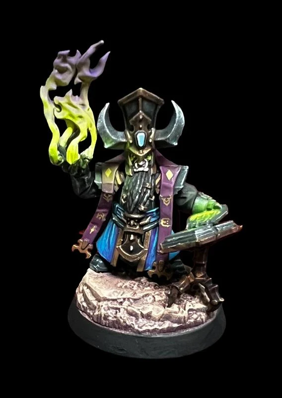 Daemonsmith der Helsmiths of Hashut in bronzegrüner Rüstung mit Hörnerhut, grün-violetter Flamme und offenem Buch auf Steinbase vor schwarzem Hintergrund