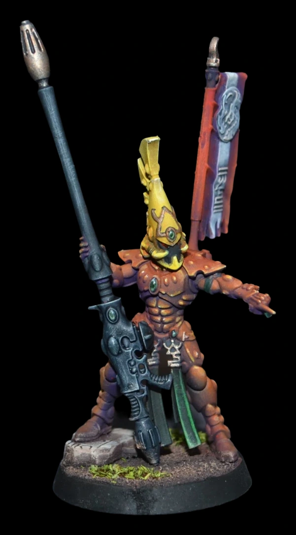 Detail: Aeldari Fire Dragon Exarch in orangeroter Rüstung mit gelbem Helmkamm und dunkler Feuerdrachen-Waffe auf steiniger Base vor schwarzem Hintergrund